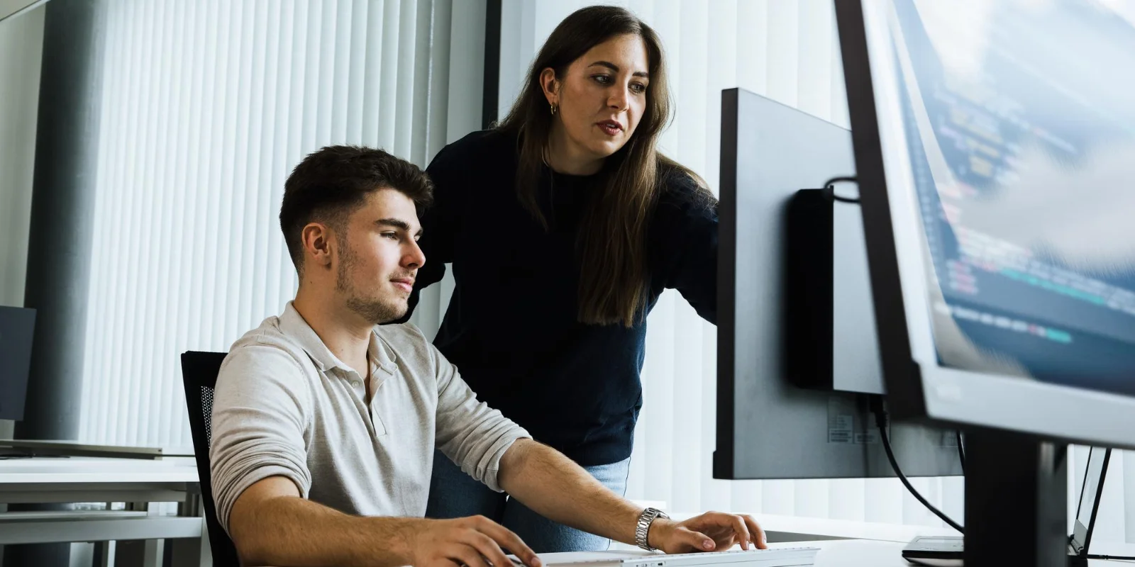 Develop certification expertise with hands-on learning and real-world application. Two professionals working together on a computer in a modern office environment, applying technical skills and collaborating on real-world development tasks.