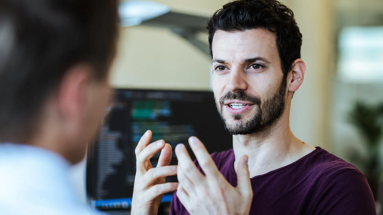 At Vector open communication and reliable reporting build trust Two people are engaged in a conversation in an Vector office. One person in the foreground faces away from the camera, while the other gestures with both hands as if explaining something.