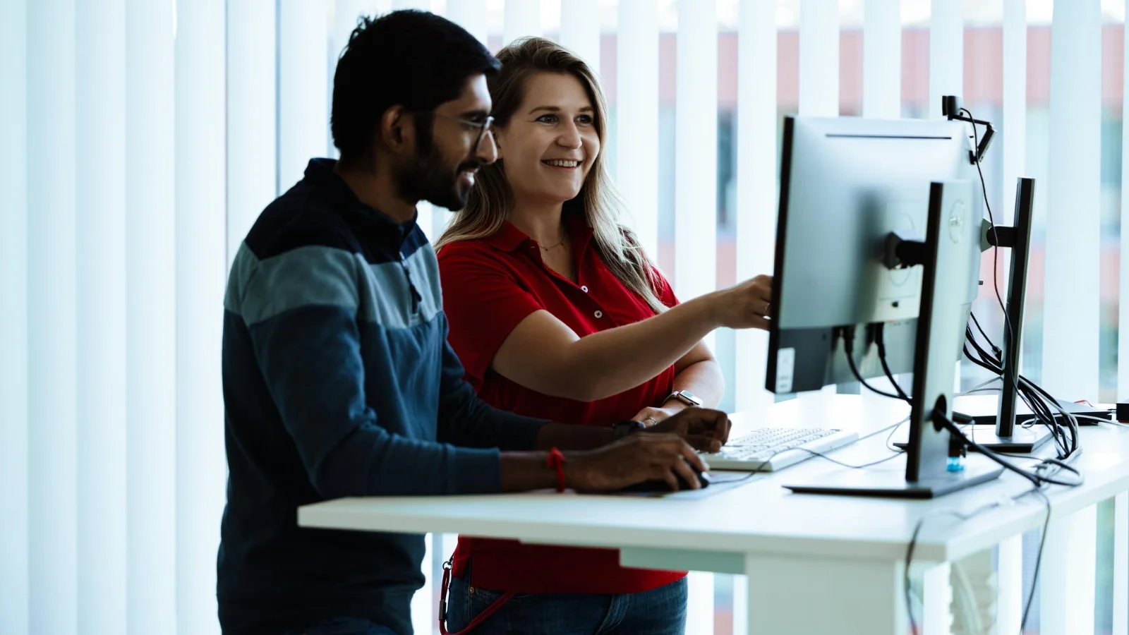 Two people working together at a standing desk and looking at computer screens in a bright office environment, representing personal contact, training support and technical guidance at Vector Academy.