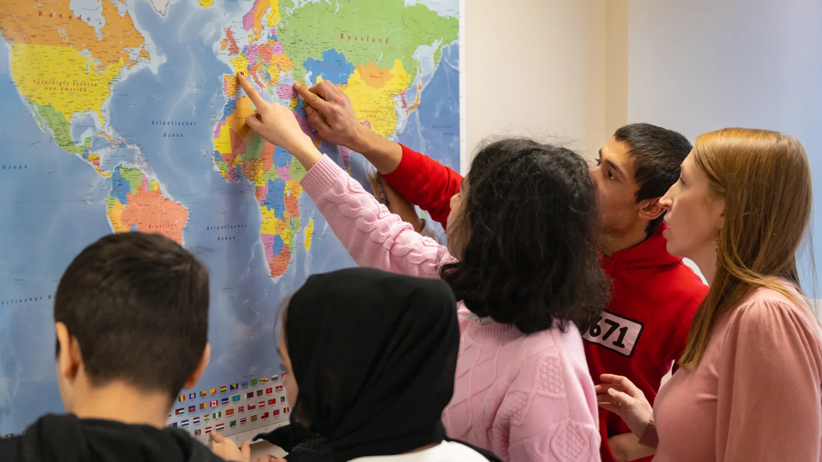 Vector supports IT education and the inclusion of children and young people. A group of children and young people stands in front of a large world map and points to different countries and regions. The students gather closely around the map, actively participating in a shared educational activity. The scene reflects learning, inclusion, and engagement in a classroom or workshop setting.