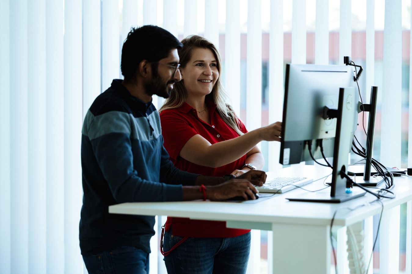 Two people working together at a standing desk and looking at computer screens in a bright office environment, representing personal contact, training support and technical guidance at Vector Academy.